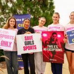 Female athletes - California Family Council Group of young women holding signs supporting girls' sports at a rally, smiling at the camera.