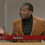 Jackson ACA 7 hearing - California Family Council Man in a brown blazer speaks at a podium with hands raised; banner reads 'ACA 7 Jackson' and 'Government preferences' in foreground.