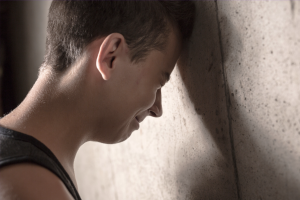 Sad boy - California Family Council Young man with his head resting against a textured wall, eyes closed in a moment of reflection or sadness.