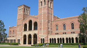 UCLA - California Family Council Brick university-style building with two tall towers, arched entry, and colonnade on a sunny day; people walking on the lawn nearby.