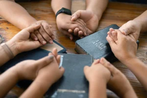 parying kids - California Family Council Several people hold hands in a circle around a Bible on a wooden table, symbolizing unity or prayer.